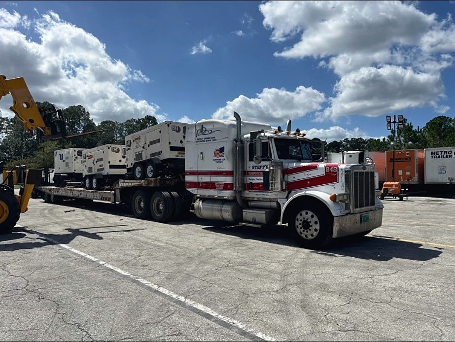 Lowboy trailer hauling mobile generators from a staging yard