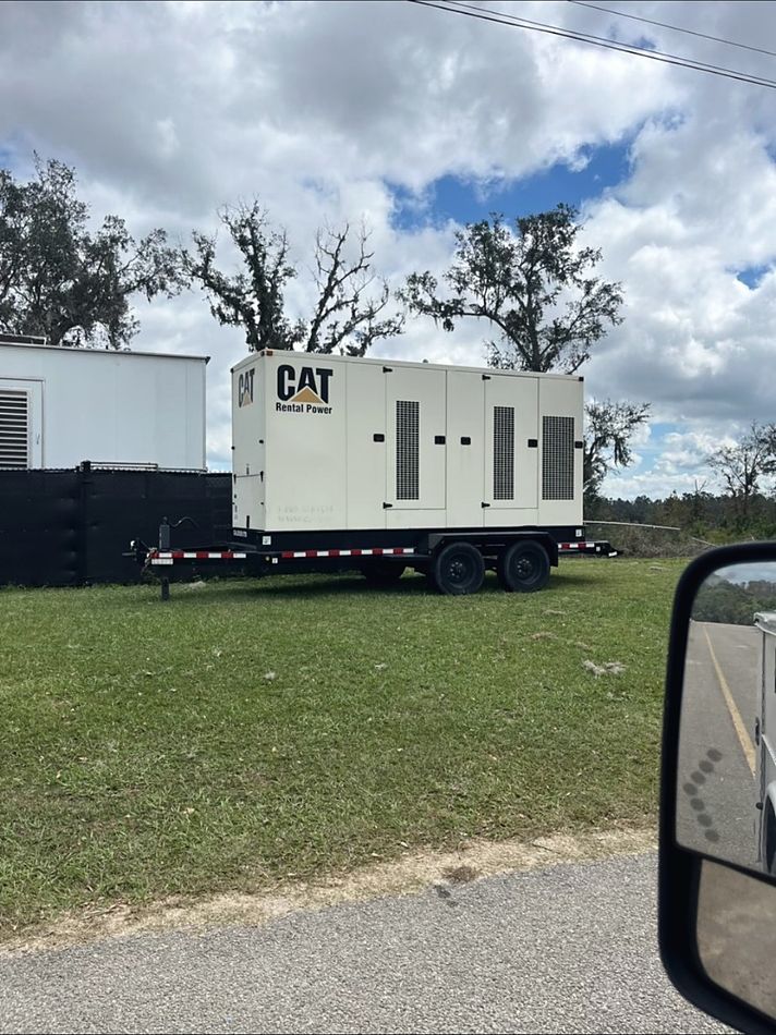 Mobile CAT generator placed beside a building surrounded by storm-damaged trees