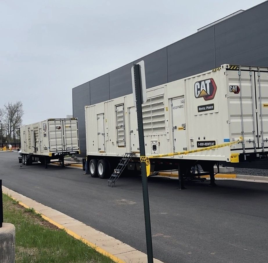 Two CAT rental power units staged on trailers alongside a commercial facility