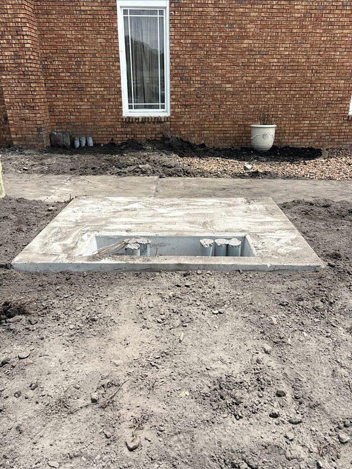 Concrete equipment pad with conduit stubs beside a brick building
