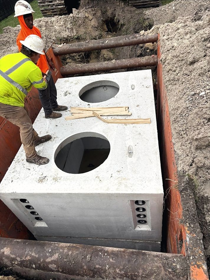 Precast concrete pull vault being set into a shored trench by the crew
